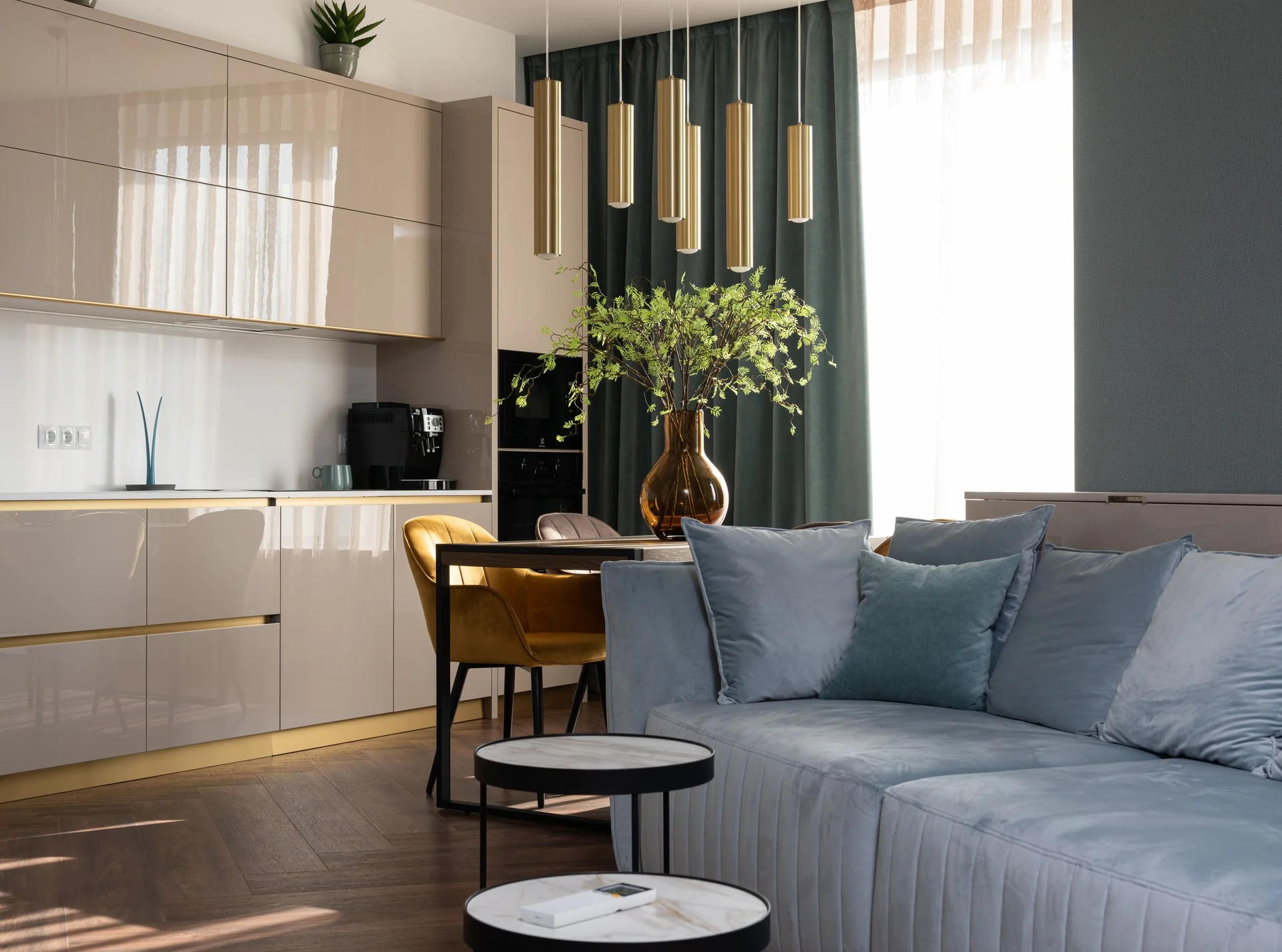Kitchen interior with light cabinets at table with flowers in vase placed near soft sofa in modern apartment with window